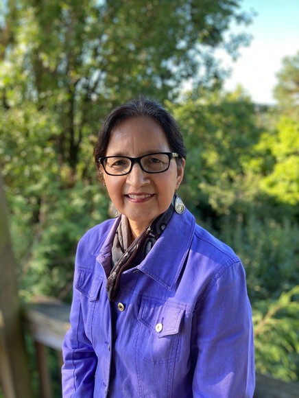 A woman wearing glasses and a purple jacket standing on a deck.