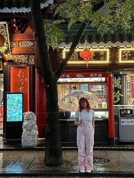 Woman holding an umbrella standing on the curb side in front of a store