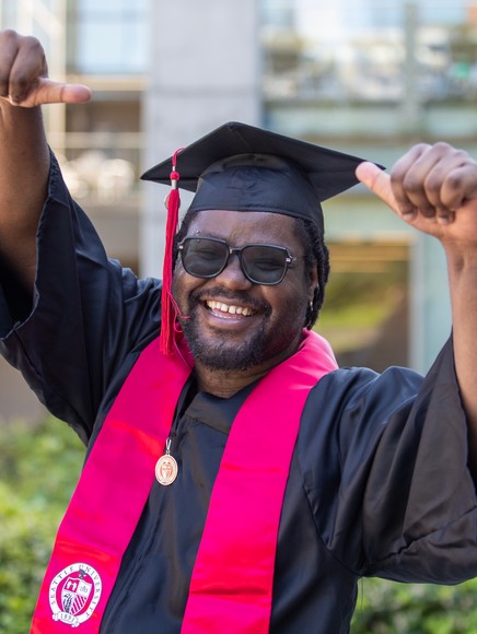 Graduating student in full grad regalia fists in air and smiling