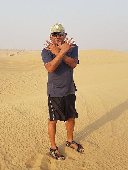 Madhu Rao doing the Red Hawk sign while standing on a dune in Dubai