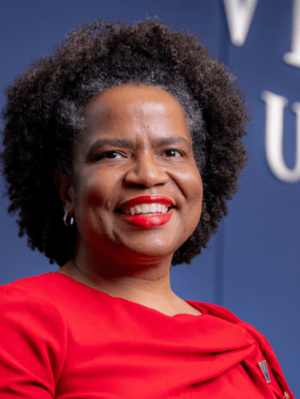 Headshot of Tia Noelle wearing a red dress. Background is blue and US flag is visible in background.