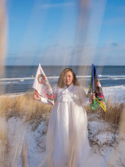 Helena Soholm holds up the five directional flags of Korean shamanism in Dronningmølle, Denmark. Photo credit: Arin Yoon