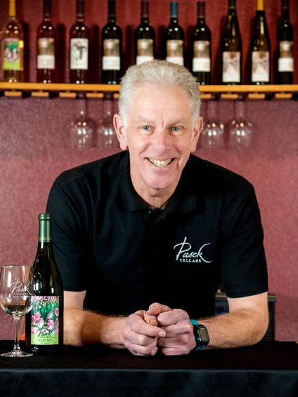 Dave James leaning on a table with wine bottles at his back
