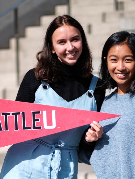 two students smiling and holding an SU pennant