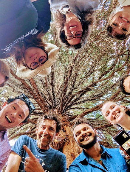 Students smile in circle looking down at camera on ground