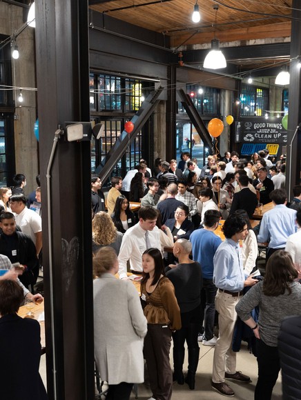 Crowd of people engaged in conversations at an indoor event with balloons and string lights.