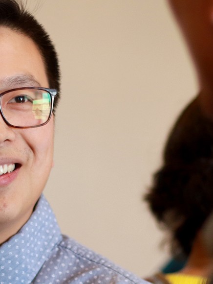 Smiling attendee wearing glasses talks with another person during a networking event.