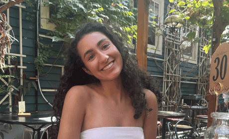 A woman sitting at a table with a drink smiling at the camera