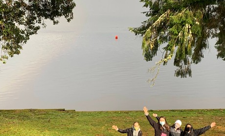 5 happy students standing outside by water and rainbow in the sky