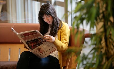 A student sits on a couch reading a newspaper