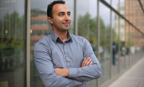 A student with his arms crossed, in front of a building