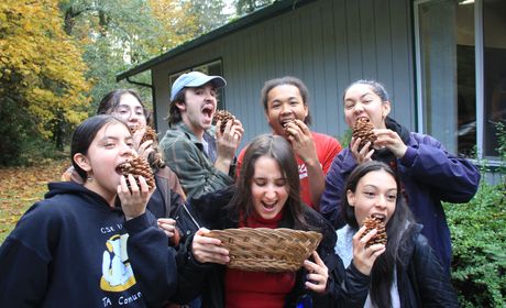 5 Students outside pretending to bite into pinecones