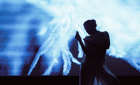 Still of Doshi mid performance with background screen.