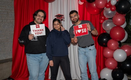 Three students pose with signs that say 