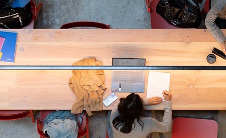 A photo from above looking down on three students studying at a long wooded table.