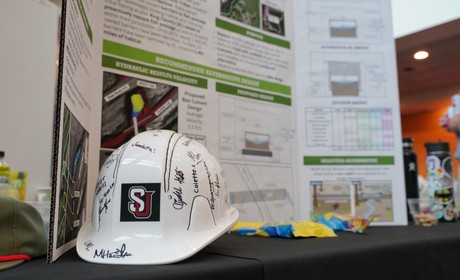 White hard hat with SU letters on front and a research poster as background