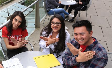 A photo of three students using their hands to make the hawk sign