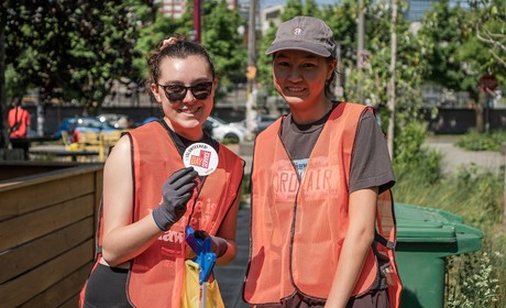 Two people posing in safety vests with one holding up an 91̽�� Day of Service sticker.