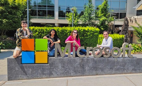 Four individuals posing with a microsoft sign at a corporate campus.