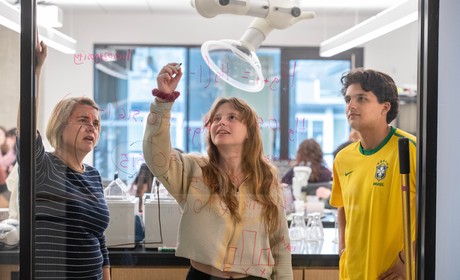 Two students and a professor write on a glass wall