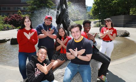 Groups of students gesturing the redhawk wings soar with their hands. The fountain is in the background.