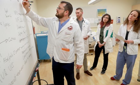 A group of people in white coats standing around a whiteboard.
