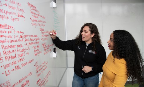 Two women standing in front of a whiteboard writing on it.