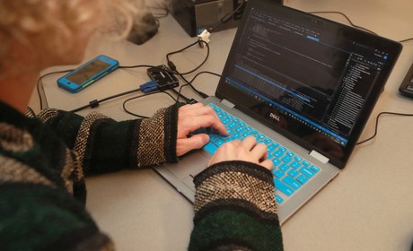 A woman working on a laptop in a room with other people.