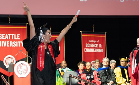 a student athlete in commencement regalia with arms raised in celebration