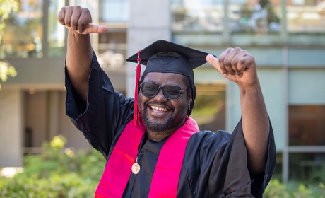 SU grad in regalia giving a smile and two thumbs up