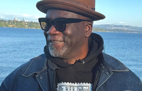 a man standing in front of a lake wearing a hat and sunglasses
