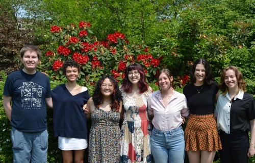 The student staff of the journal in front of red flowering bush