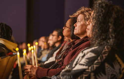 Audience members holding candles looking at a stage