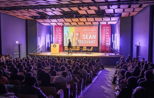 An auditorium with a full audience and a speaker