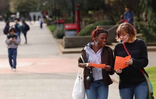 Two students speaking while looking at flyers and walking through campus