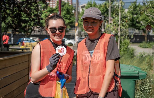 Two people posing in safety vests with one holding up an SU Day of Service sticker.