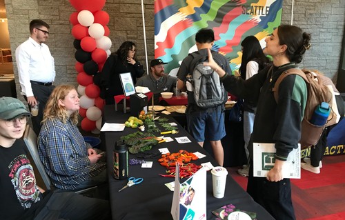 Image of students talking. There is a table with black linen in the middle with vegetables on top of it.
