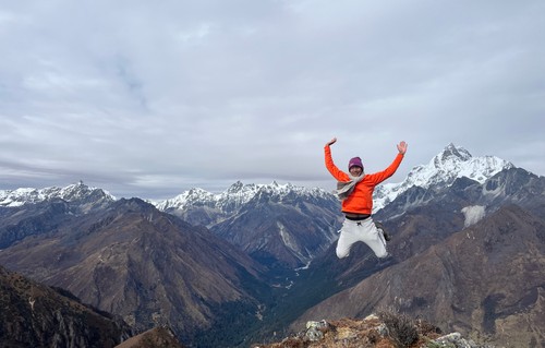 Man jumping on a mountain-top in front of mountain range