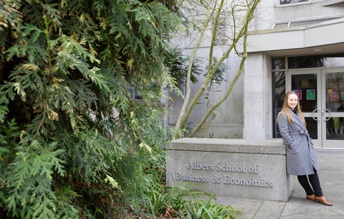 A student leaning against signage of the Albers School of Business and Economics
