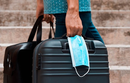 Hands of man carrying a face mask along with a suitcase