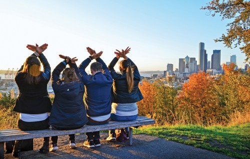 Students displaying hawk hands while sitting at a scenic overlook of Seattle