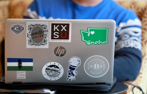 A man sitting in front of a laptop with stickers on it.