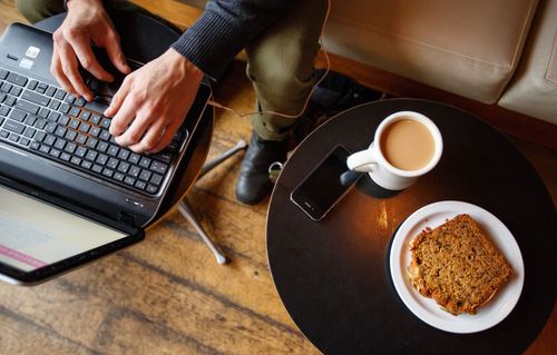 Person using a laptop with coffee and pastry