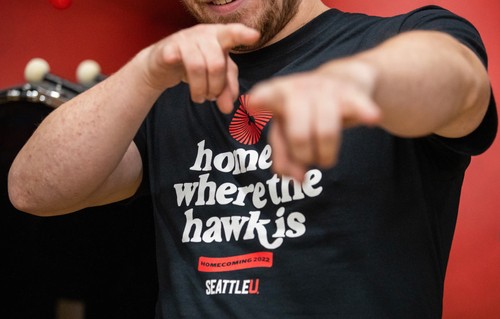 A man in a Seattle University t-shirt pointing at the camera