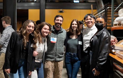 A group of five smiling people posing for a photo at an indoor social event.
