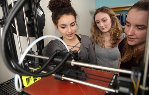 Three students look at a 3d printer.