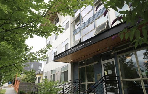 Four-floor modern apartment building with a covered entrance on a tree-lined neighborhood street.