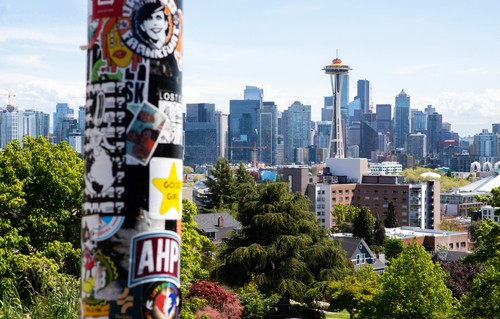 A tall pole with stickers on it and a city in the background.