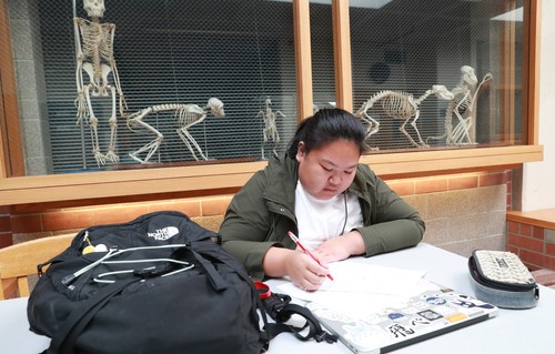 A woman sitting at a table writing on a piece of paper.