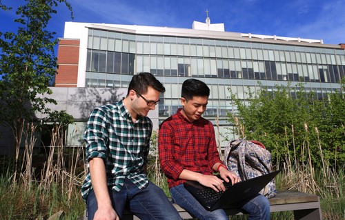 Two students sitting on a bench in front of a building.
